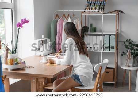 Female tailor with cup of coffee drawing sketch at table in atelier
