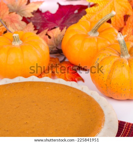 Closeup of a whole pumpkin pie with pumpkins and autumn colored leaves in background