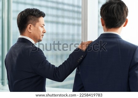 two asian business men standing by the window chatting talking Royalty-Free Stock Photo #2258419783