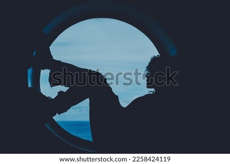 Silhouette of a woman boat passenger having relax sitting on a big window porthole with sea ocean waves in background outside. People in travel trip lifestyle. Transport on the ocean. Wanderlust Royalty-Free Stock Photo #2258424119