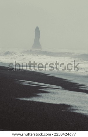 Rock pillar on black beach landscape photo. Beautiful nature scenery photography with fog on background. Idyllic scene. High quality picture for wallpaper, travel blog, magazine, article