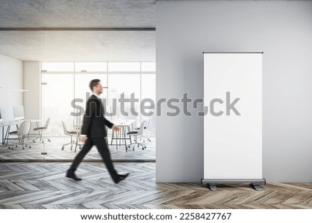 Businessman walking in modern glass office interior with empty mock up banner on wall, wooden flooring, furniture, window with city view and other objects Royalty-Free Stock Photo #2258427767
