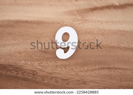 White number 9 on a brown and light brown wooden background.