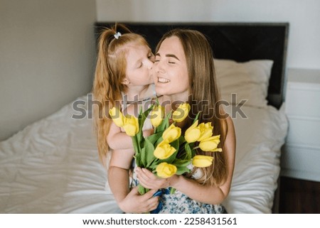Daughter congratulates mother and gives bouquet of yellow tulip flowers at home. Mother's day concept. Mom and child girl hug and kiss. Greeting card for International Women's Day. Closeup.