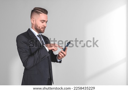 Inspired handsome businessman in formal wear standing holding smartphone near empty white wall in background. Concept of pleased business person, dreaming man, social media, mobile application