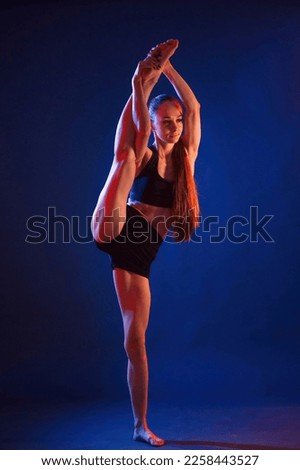 Raising up the leg, exercise. Beautiful muscular woman is indoors in the studio with neon lighting.