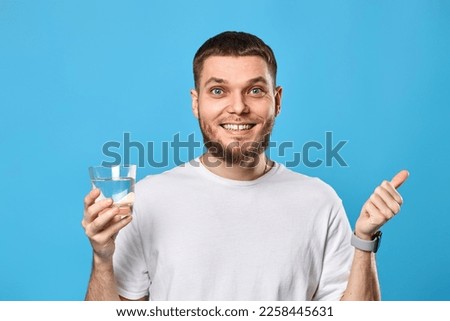 man in white t-shirt with drinking glass of water pointing to the side Royalty-Free Stock Photo #2258445631