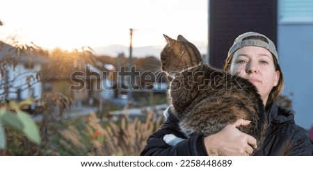 
Woman in cool baseball cap holds cat in her arms in the garden