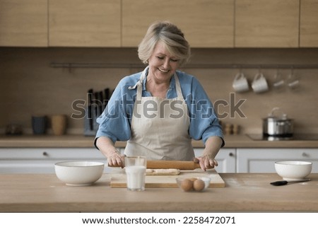 Happy senior cook blogger woman baking in home kitchen, rolling dough on floury board, preparing bakery food dessert, smiling, laughing, shooting culinary workshop Royalty-Free Stock Photo #2258472071