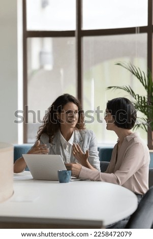 Two happy engaged business professionals women brainstorming on online project at laptop, speaking, discussing creative ideas, plan, strategy, task, chatting at work desk in office Royalty-Free Stock Photo #2258472079