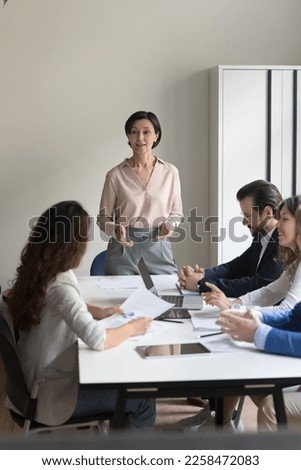 Confident senior corporate coach woman giving seminar to business team. Female director, box, CEO talking with employees on office meeting, discussing project, instructing. Vertical shot Royalty-Free Stock Photo #2258472083