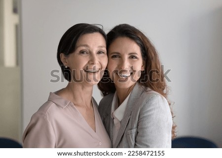 Cheerful senior middle aged mom and pretty brunette daughter woman posing cheek to cheek together, standing close with face touches, looking at camera, smiling, laughing, hugging Royalty-Free Stock Photo #2258472155