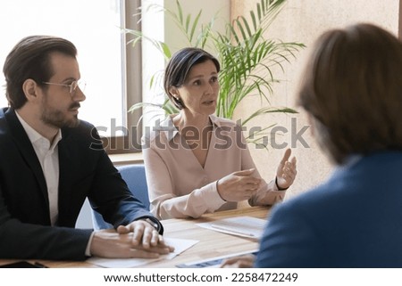 Serious engaged business leader woman talking to colleagues on office meeting, discussing project strategy, telling ideas, offering solutions, problem solving, sitting at table Royalty-Free Stock Photo #2258472249
