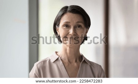 Positive confident pretty mature business leader woman head shot portrait. Senior black short haired lady looking at camera, smiling, posing in office indoors. Banner shot