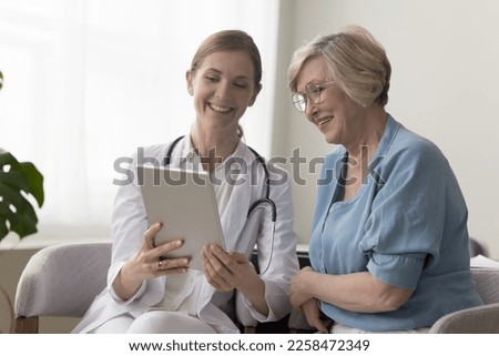 Positive practitioner doctor showing tablet screen to elder 70s patient woman, explaining checkup result, medical screening, roentgen electronic shot, giving consultation on appointment Royalty-Free Stock Photo #2258472349