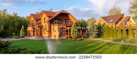 Modern wooden eco house villa facade luxury big house. Timber cottage with with green lawn water sprinkler, paved footpath and blue sky background. Landscaping design, garden watering and maintenance Royalty-Free Stock Photo #2258475503