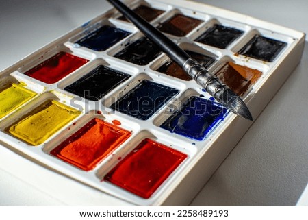 A set of watercolor paints and a brush for drawing on a white table Royalty-Free Stock Photo #2258489193