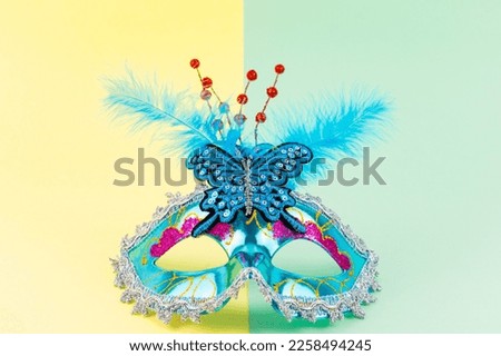 Front view of a Mardi Gras turquoise mask with yellow and green background. Colorful blue costume accessory with feathers for party and Venice carnival. Horizontal banner with copy space. 