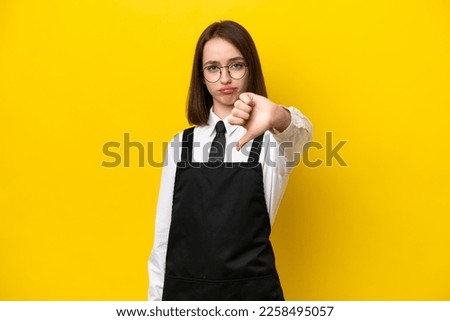 Young Ukrainian waitress woman isolated on yellow background showing thumb down with negative expression