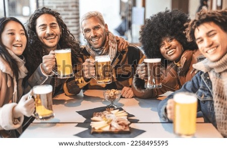 A group of multiracial friends raise their beer mugs in celebration at a pub event. Friends coming together and enjoying a night out.