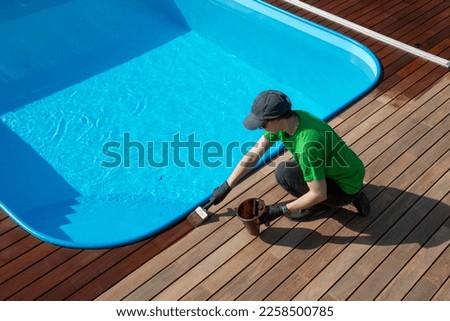 Seasonal restoration of wooden deck around the swimming pool, decking oil application Royalty-Free Stock Photo #2258500785