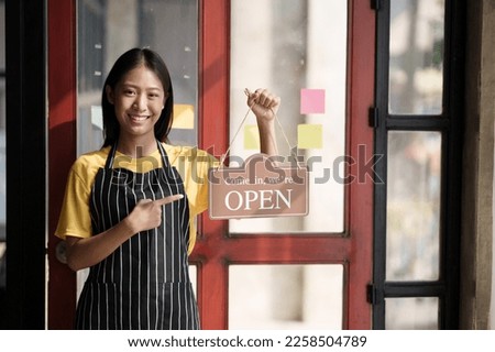 Small business owner smiling while turning the sign for the opening of the shop. Close up of woman€™ hands holding sign now we are open support local business.
