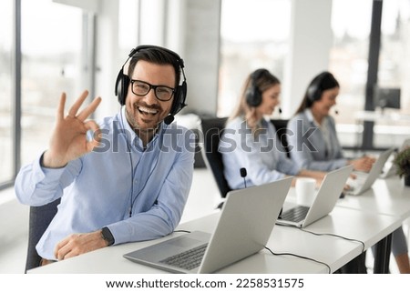Portrait of handsome bearded business man with headset showing OK sing at call center office Royalty-Free Stock Photo #2258531575