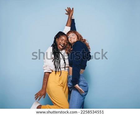 Two best friends dancing and having a good time together in a studio. Happy young women enjoying themselves while standing against a blue background. Female friends making cheerful memories. Royalty-Free Stock Photo #2258534551