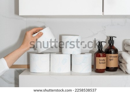 cropped shot of female hand hold toilet tissue roll near body care products in dispenser bottles in bathroom with light interior, storage concept at home Royalty-Free Stock Photo #2258538537