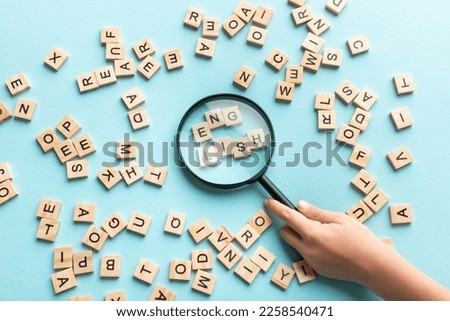 Square letter tiles with magnifying glass against blue background. Search for words and information concept.
