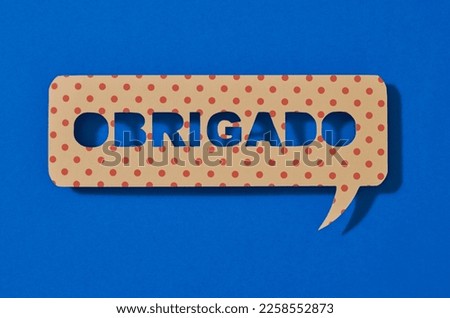 a paper sign in the shape of a speech bubble with the text thank you written in portuguese, on a blue background