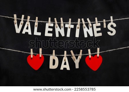 Clothes pegs pin and valentine's day text red wooden hearts on rope on white black background Valentines day concept.
