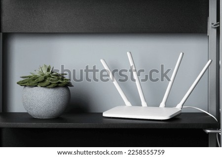 New white Wi-Fi router near potted plant on black shelf Royalty-Free Stock Photo #2258555759