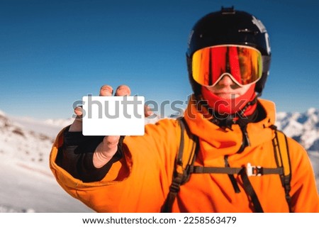 Snowboarder or skier holding blank lift pass in hand, portrait with mountain in the background. Ski pass in hand close-up