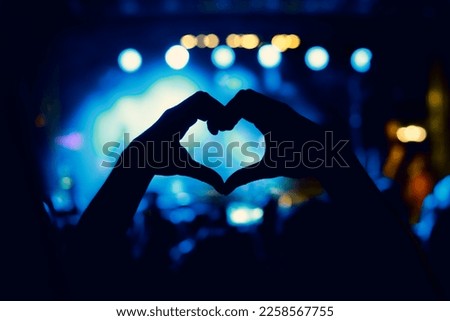 A person is making a heart sign during a concert of a favorite music band. Black silhouette
