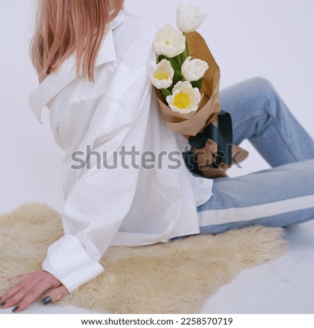 Woman in white shirt sitting and holding a bouquet of white tulips in her hands. Feminine. White shirt. Gift concept for woman, love, birthday, 8 March, mother day. 
