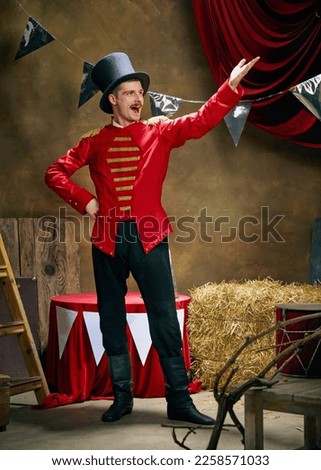 Showman. Vintage portrait of male retro circus entertainer expresses rejoice and announces start of show over dark retro circus backstage background. Concept of emotions, art, fashion, style Royalty-Free Stock Photo #2258571033