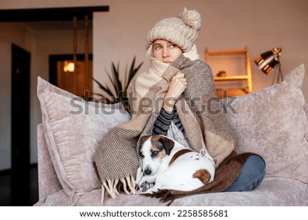 Frozen. Sad woman sit on couch at freezing cooled house in warm cap and blanket shiver tremble with cold. Unhappy middle aged lady spend time at home feel bad suffer of heating system problems Royalty-Free Stock Photo #2258585681