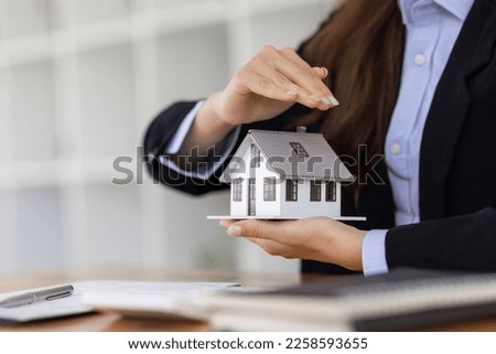 Wooden toy house with real estate agent Asian business woman signs a purchase contract mortgagefor rent sell insurance or loan for a home, Real estate concept.