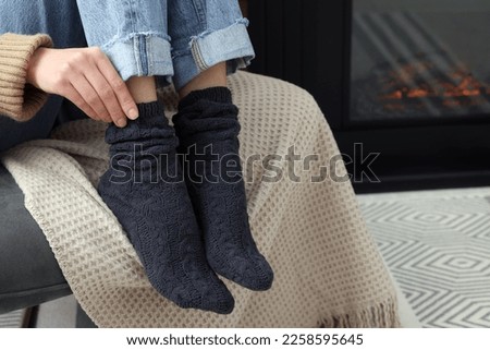 Woman in warm socks relaxing near fireplace at home, closeup