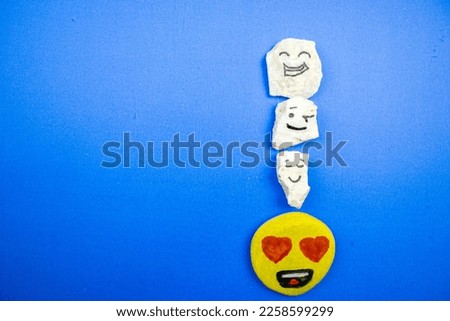 Image with heart eyed happy stone, happy white stone, smiley white stone and cool stone placed on the right of a blue background.