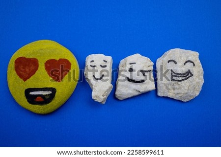 Image with heart eyed happy stone, happy white stone, smiley white stone and cool stone placed over blue background.