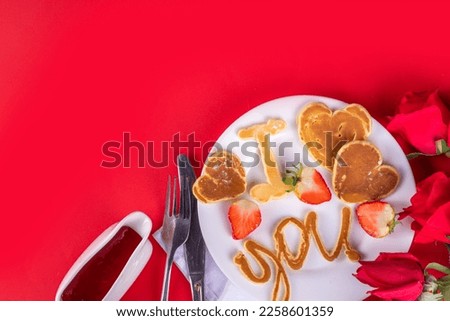 Cute Valentine pancakes, sweet homemade butter cake shaped in form of I love you, Be my heart inscription. Breakfast or gift idea for Saint Valentine day, with strawberry and syrup. on red background