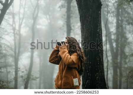 Beautiful passionate woman taking pictures outdoors with a digital camera. Hiking and photographing on a cold day