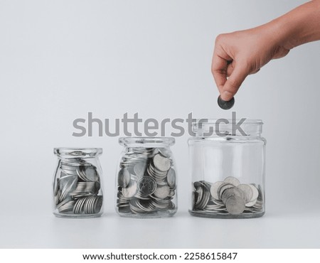 Woman hand with money coins in clear glass on white background, Business investment growth concept, saving concept, Hand putting coin in clear jar over white background. Copy space. Royalty-Free Stock Photo #2258615847