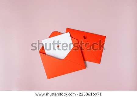 two red envelopes on a pink background lie in the center, one is open, a white sheet of paper sticks out of it, a letter with a heart, the other letter is closed