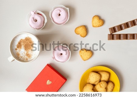 the mood of valentine's day, on a beige background there is a mug of cappuccino, a red box with a gift, candles, photos of a couple from a photo booth, heart-shaped cookies, pink marshmallows