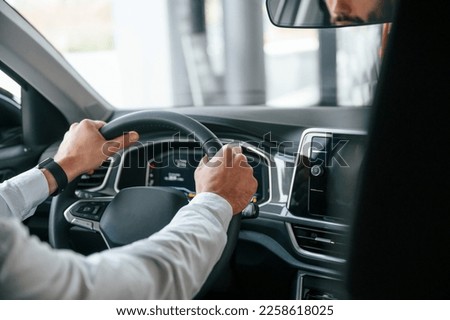 Test drive. Young man in white clothes is in the car dealership. Royalty-Free Stock Photo #2258618025