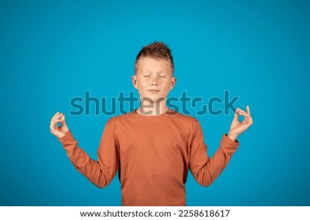 Zen. Calm Preteen Boy Meditating With Closed Eyes Over Blue Background, Relaxed Male Child Practicing Yoga Meditation, Keeping Hands In Mudra Gesture While Posing In Studio, Copy Space
