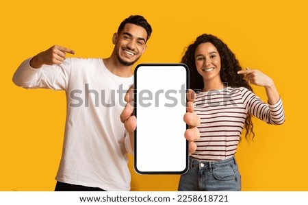 Place For Ad. Cheerful Middle Eastern Couple Demonstrating Big Blank Smartphone With White Screen For Mockup And Pointing At It, Happy Arab Man And Woman Advertising New Mobile App Or Website Royalty-Free Stock Photo #2258618721